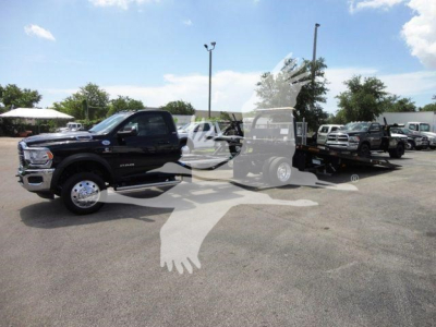 Ram 5500 SLT pickup truck in a dealership lot with rollback tow truck in background, black exterior, chrome wheels, daytime.