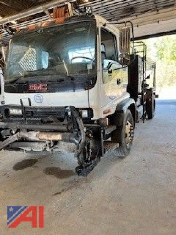 GMC T7500 pothole patcher truck front view showing damaged plow and equipment mounting under a shelter.