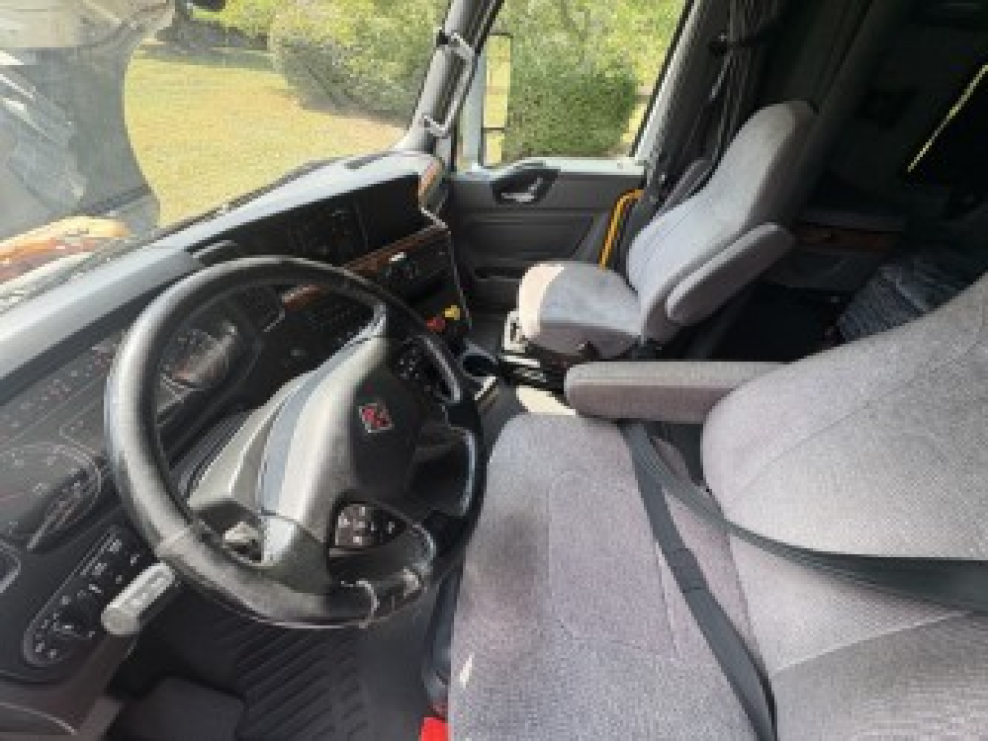Truck cabin interior showing steering wheel with International logo, dashboard, and two seats inside a sleeper cab.