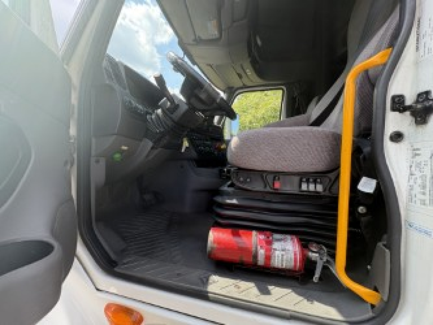 Cab interior of a 2021 International LT625 truck showing driver seat, steering wheel, dash controls, and a red fire extinguisher on the floor.