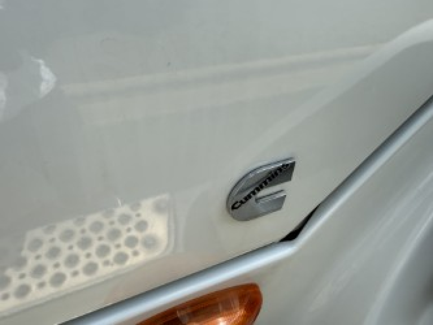 Trucks wheel area showing International logo emblem on side of a cab, with treaded step and orange turn signal lens.
