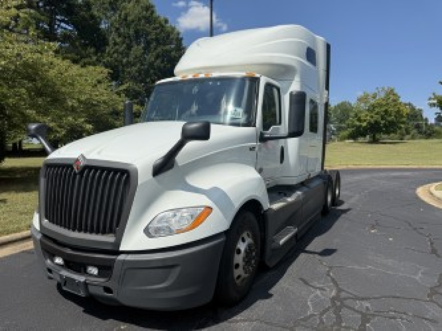 Truck cab with a large black grille and white exterior showing a sleeper tractor for International LT625, front view in a parking lot.