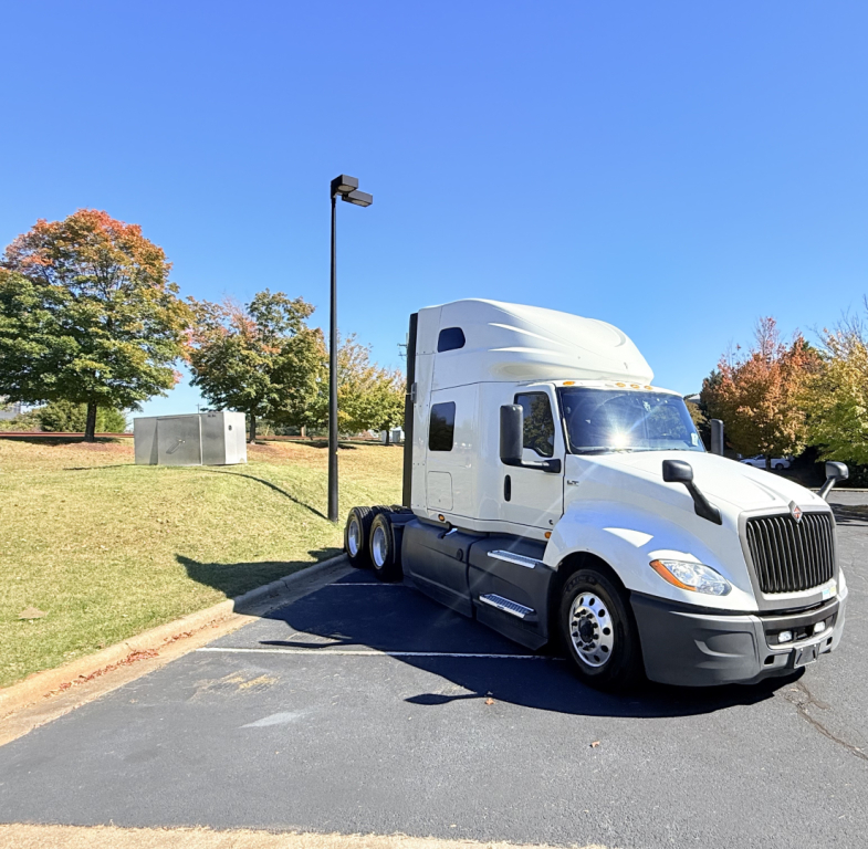2021 International LT625 tractor-trailer in a parking lot, white cab, sleeper with two axles, side view, clear blue sky.