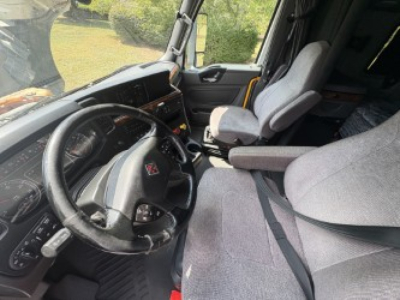 Truck cabin interior showing steering wheel with International logo, dashboard, and two seats inside a sleeper cab.