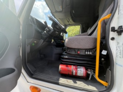 Cab interior of a 2021 International LT625 truck showing driver seat, steering wheel, dash controls, and a red fire extinguisher on the floor.