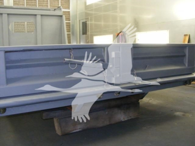 Dump truck bed component showing reinforced steel side panel and undercarriage in blue; label text not visible.