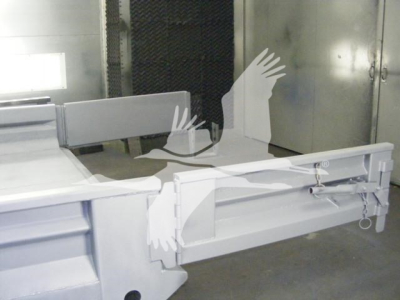 Dump truck bed or trailer hitch assembly in a workshop, with metal rails and latching mechanism visible.