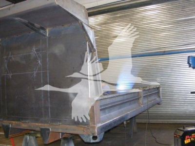 Dump trailer side view showing metal dump bed and side panel with a utility stripe; no legible model numbers or text visible on the equipment.