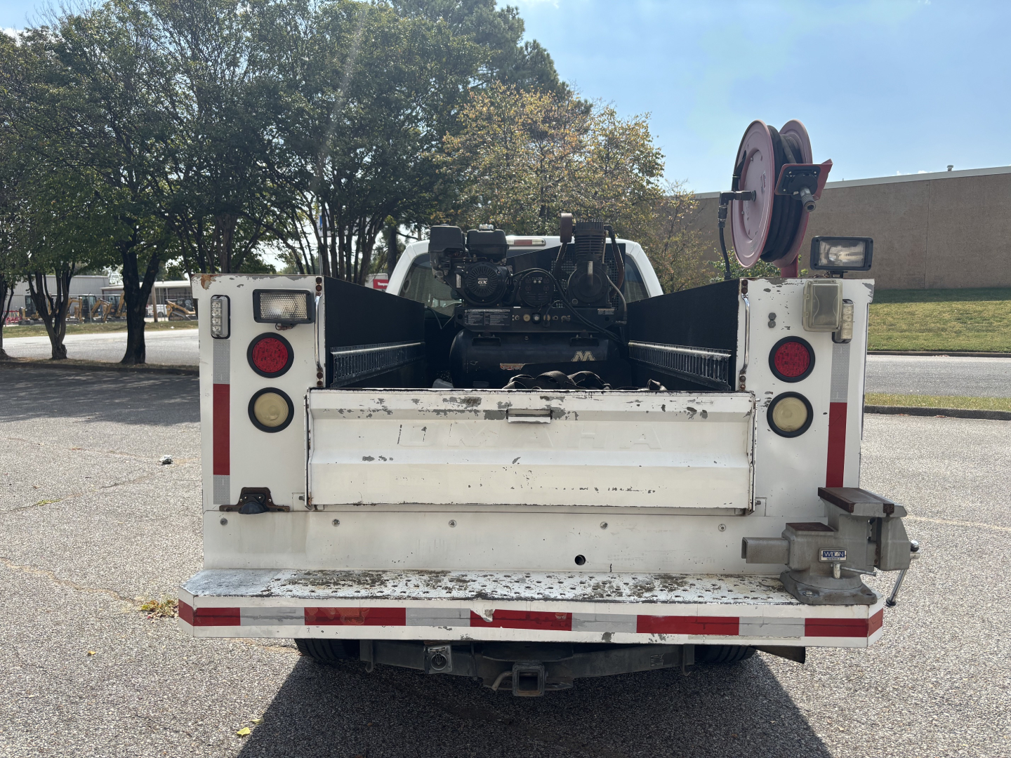 Rear view of a white Ford F-250 service/utility truck with racks and a reel on the right side, showing taillights, bumper, and hitch.