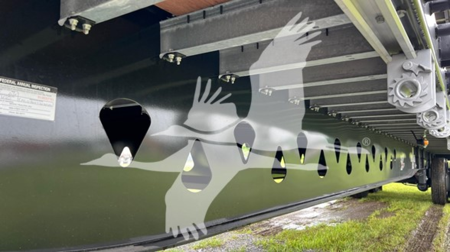 Manac steel flatbed trailer side with cutout pattern of hands; metal side panels with small warning label and perforations along lower rail.