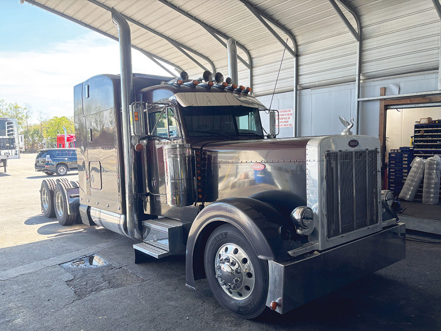 Peterbilt 379 UltraCab Extended Hood conventional truck in service bay showing chrome grille, sleeper cab, dual rear axles, and large front wheels.