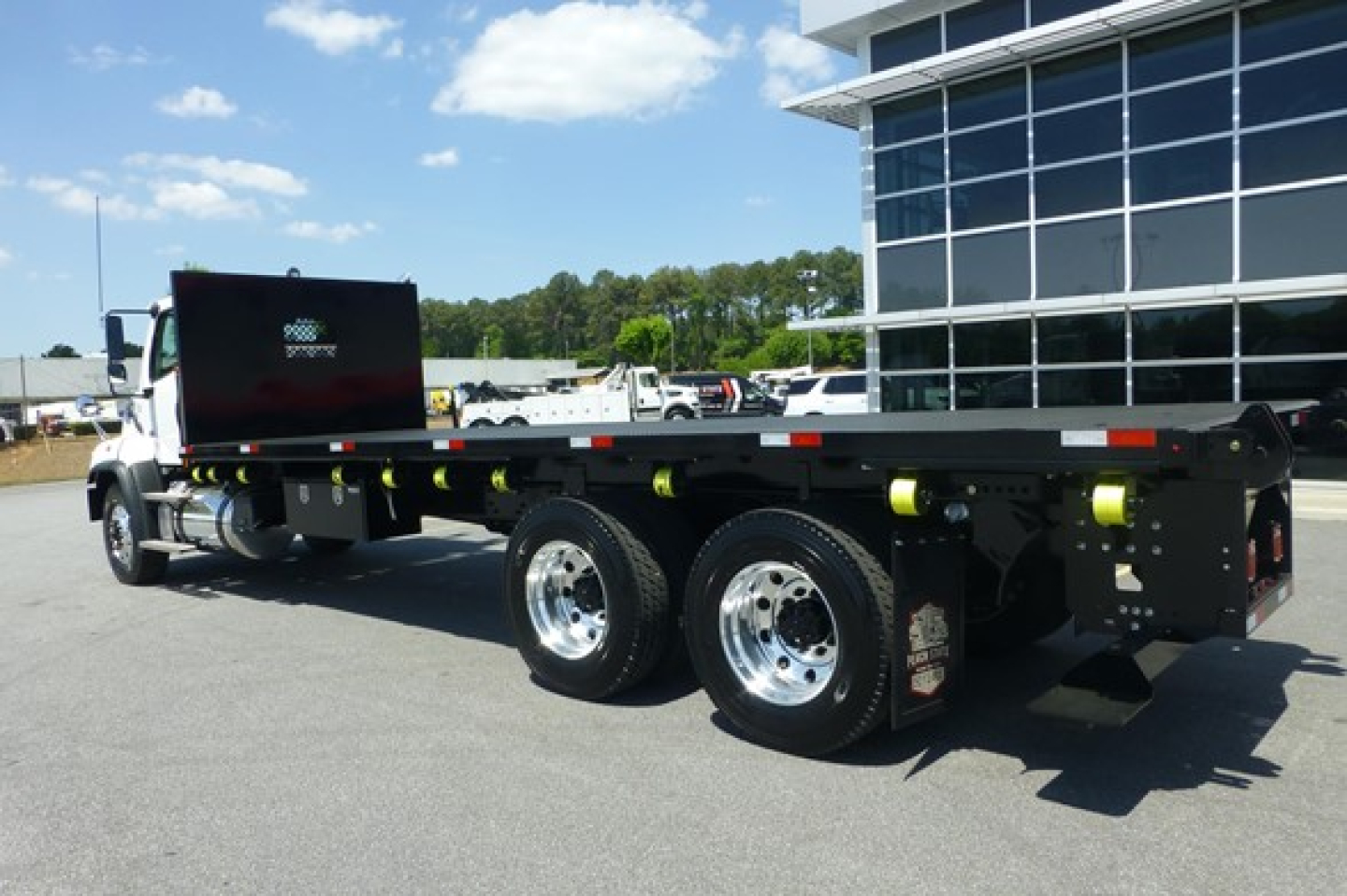 Freightliner 114SD flatbed truck shown in side view with dual rear axles and raised black flatbed, chrome wheels, and safety markers.