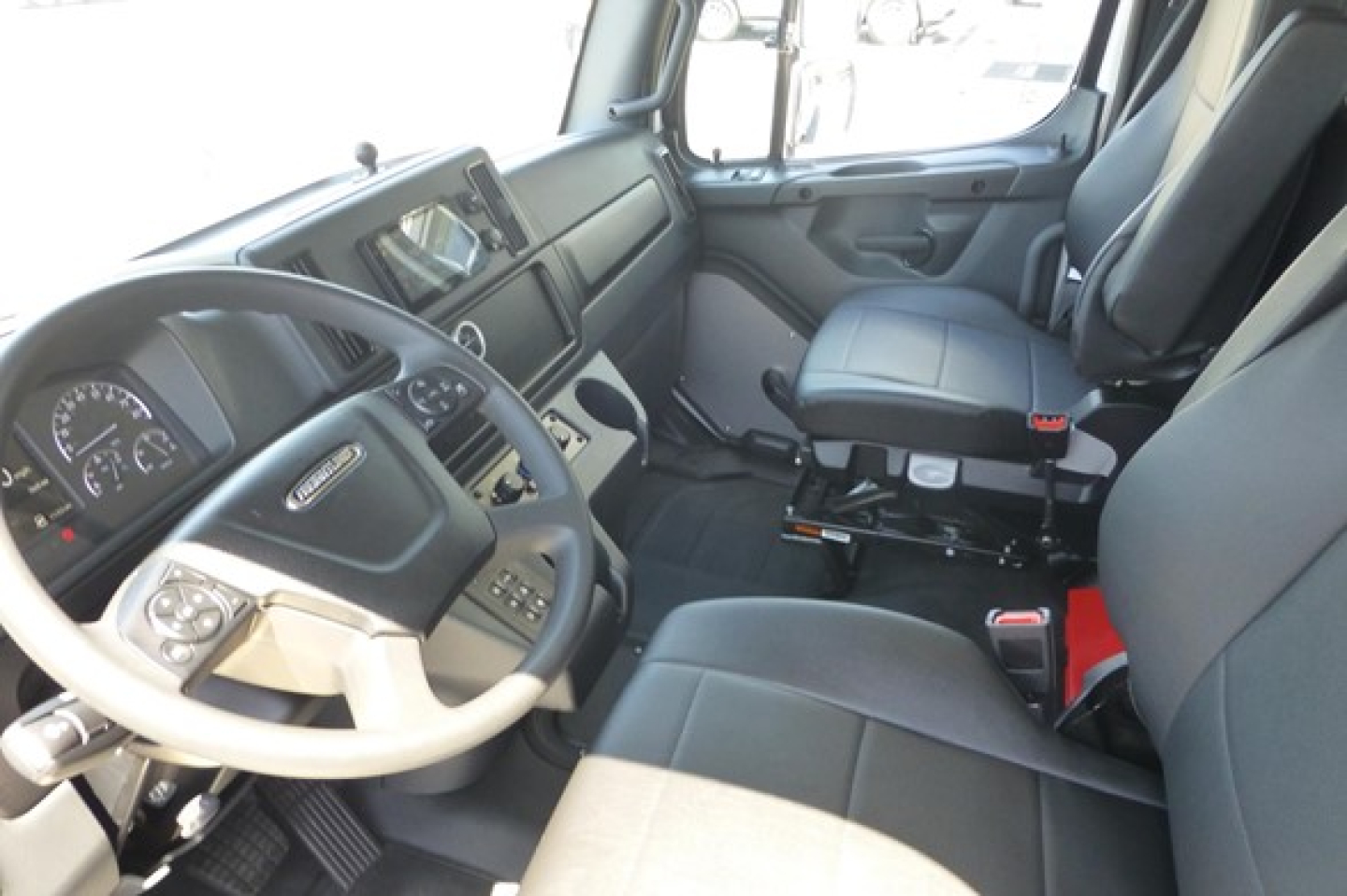 Freightliner truck cab interior showing steering wheel, dashboard, and driver seat with modern controls.