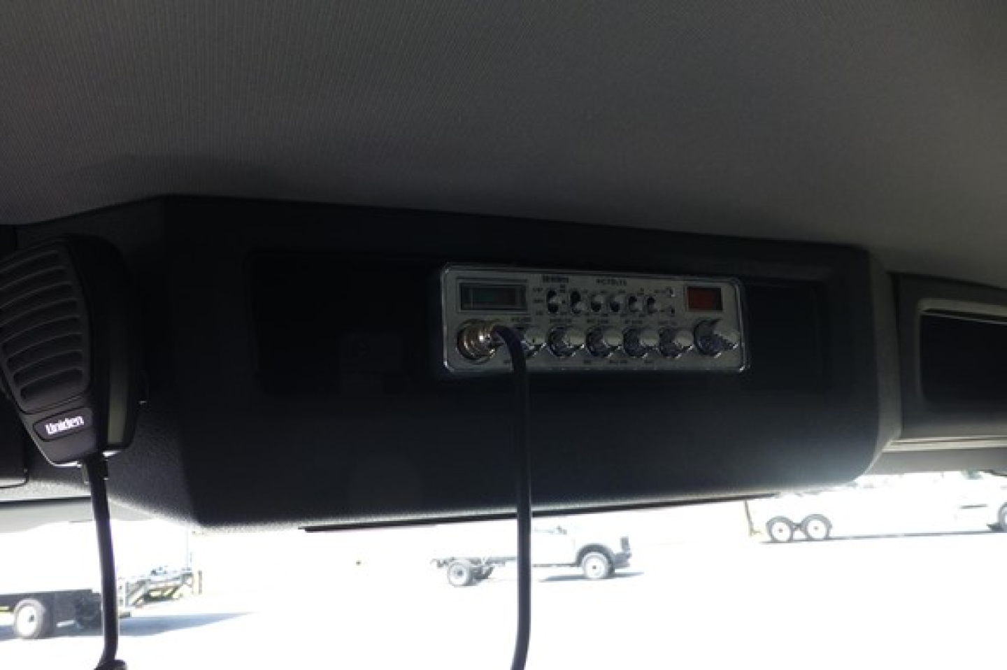 Truck interior ceiling with a silver CB radio unit and connected microphone, mounted in overhead console.