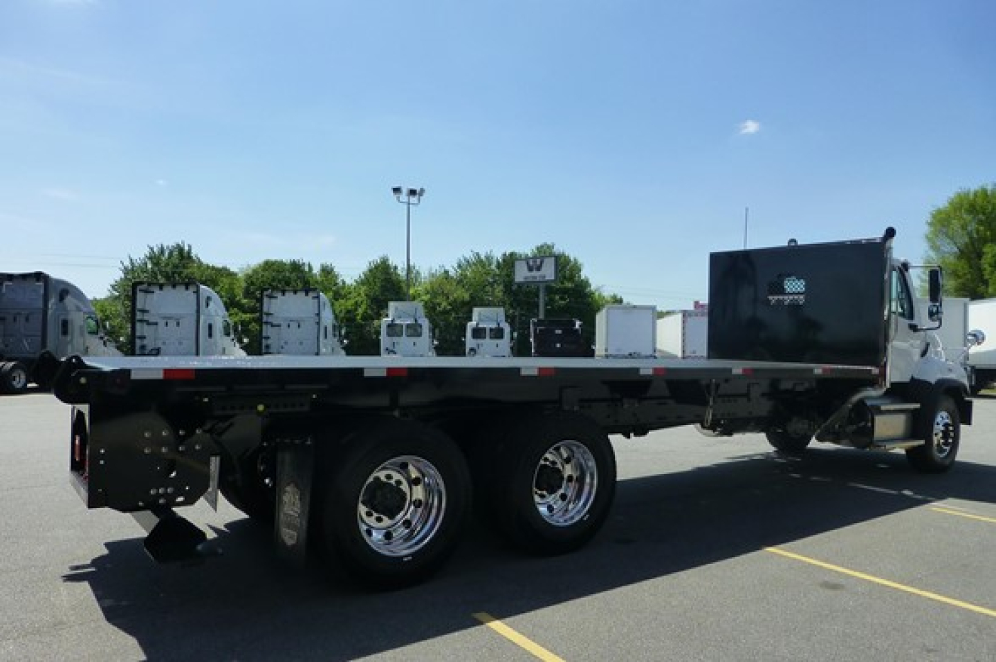 Flatbed truck chassis showing dual rear axles and a black tool/storage box toward cab; Freightliner 114Sd Plus likely new, VIN and stock not visible on image.