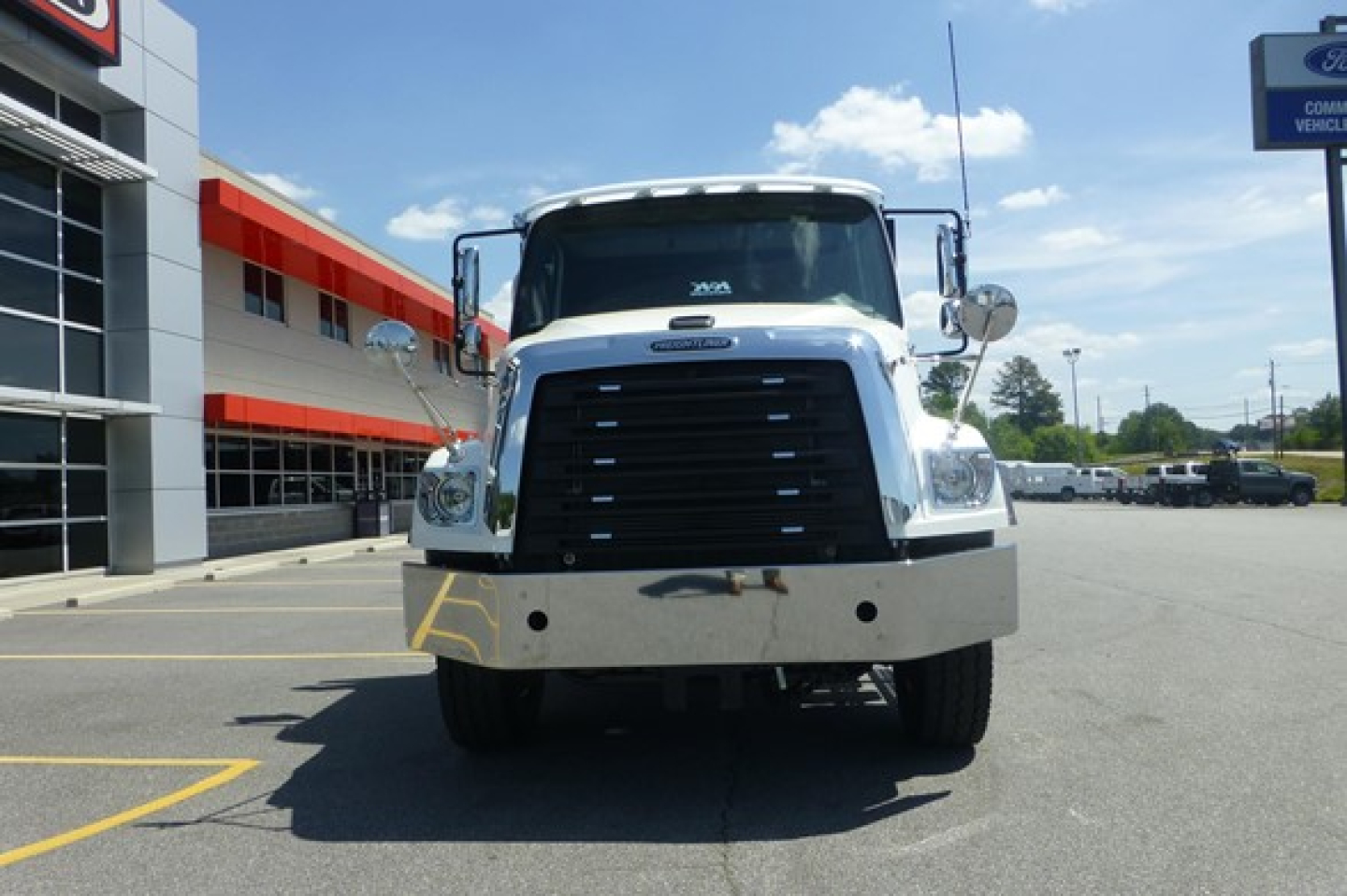 Freightliner 114SD Plus flatbed truck front view showing large black grille and chrome bumper.