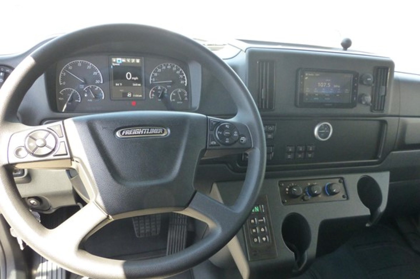 Freightliner 114SD Plus truck interior showing steering wheel, dashboard gauges, and center console with radio and climate controls.