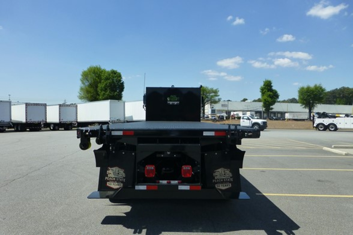 Freightliner 114SD Plus rear view showing flatbed with dual rear lights and bumper, in a dealership lot.