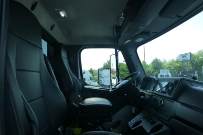 Cab interior of a Freightliner 114SD Plus truck showing driver seat, steering wheel, dashboard, and large front windshield.