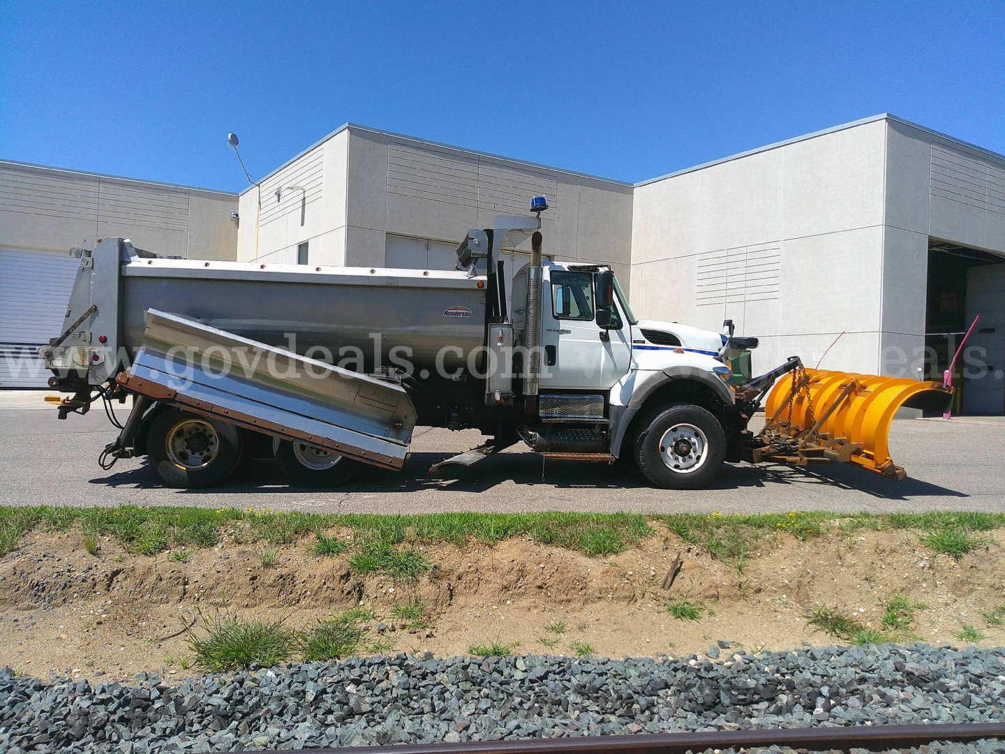 Truck with a plow attachment and dump bed in a parking lot, International chassis, side view showing plow blade and hydraulic components.