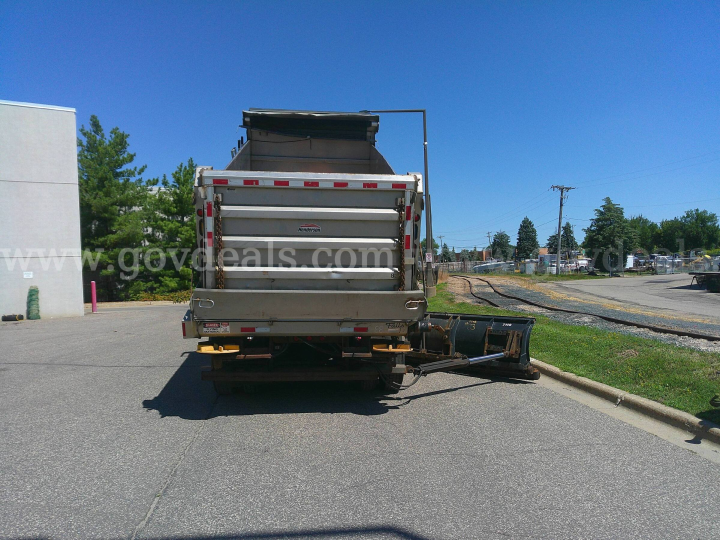 Rear view of a white dump truck with a plow attachment on the ground behind it. No visible text on the truck from this angle.