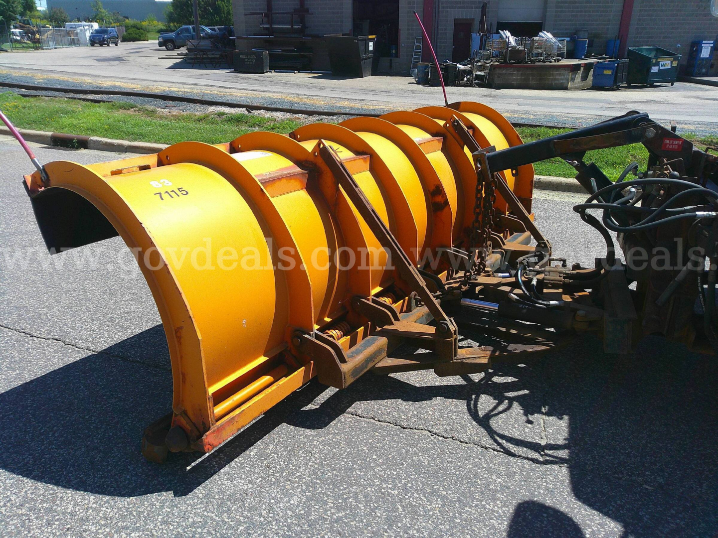 Snow plow attachment showing yellow rotating blades and hydraulic components.