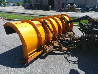 Snow plow attachment showing yellow rotating blades and hydraulic components.