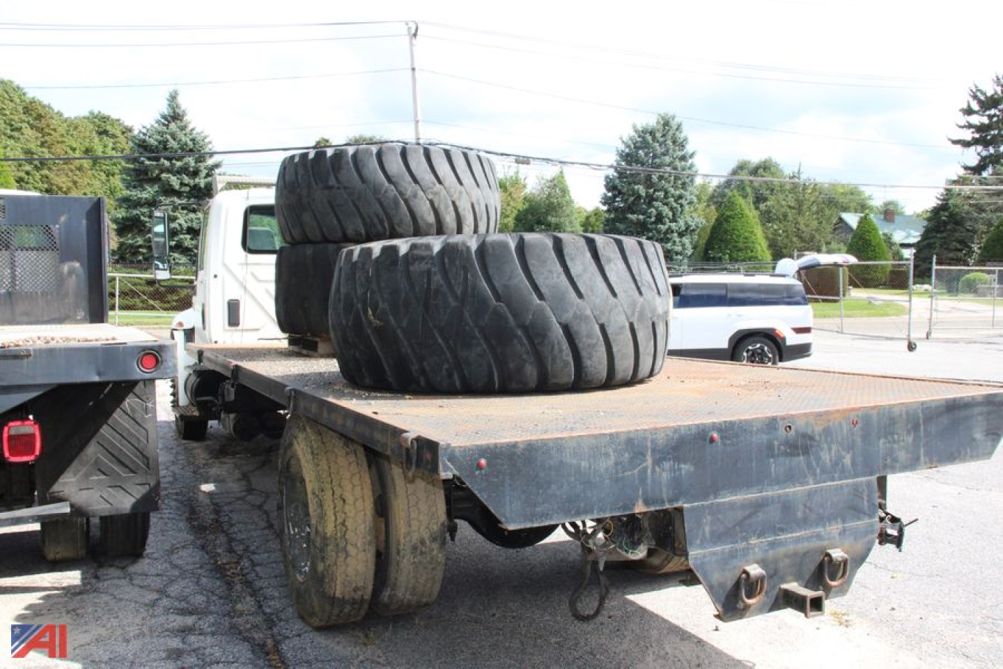 Flatbed truck bed with two large off-road tires stacked near the cab area, wheel fenders, and a chain hitch visible.
