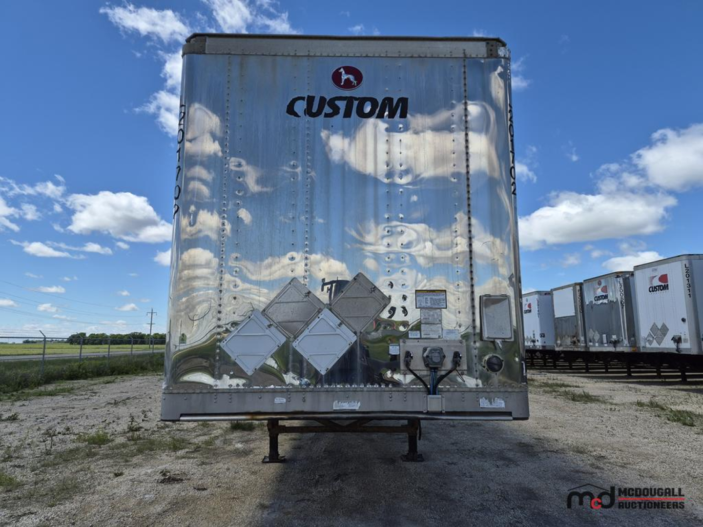 Trailer rear showing Custom logo on a shiny aluminum surface with scattered equipment decals and a support leg base.