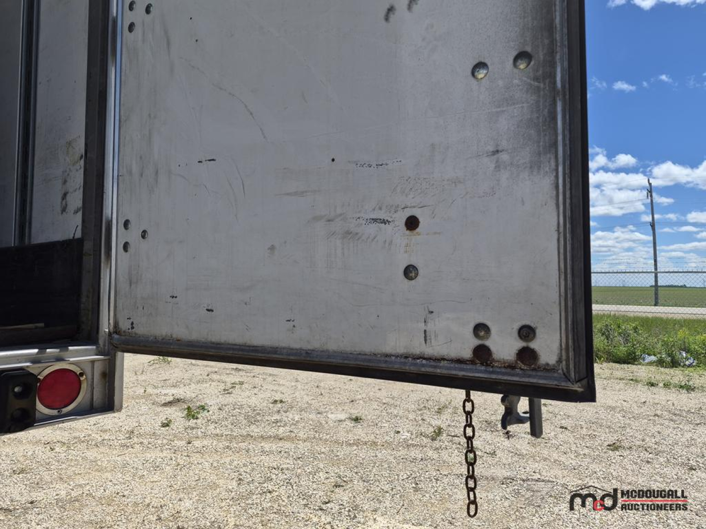 Trailer rear door edge with chain and hinge pins visible, metal surface with scuffs and rivets.