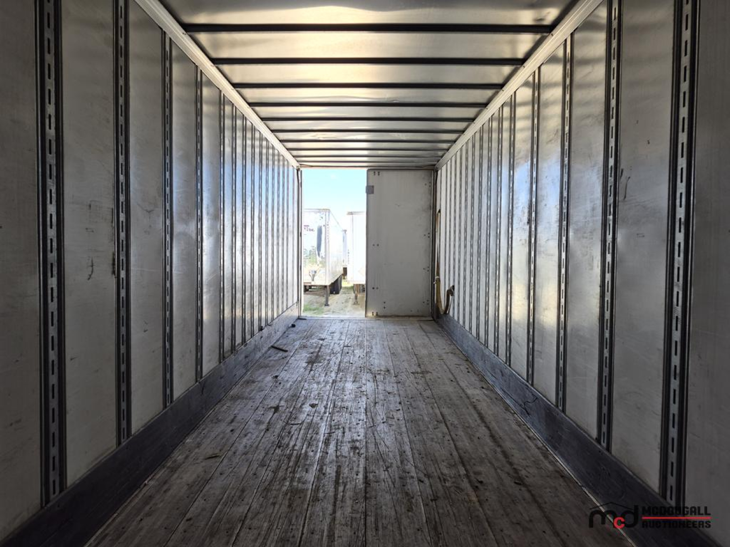 Trailer interior view of a 53' Great Dane dry van semi-trailer showing metal side rails, plywood floor, and open rear with light at the end.