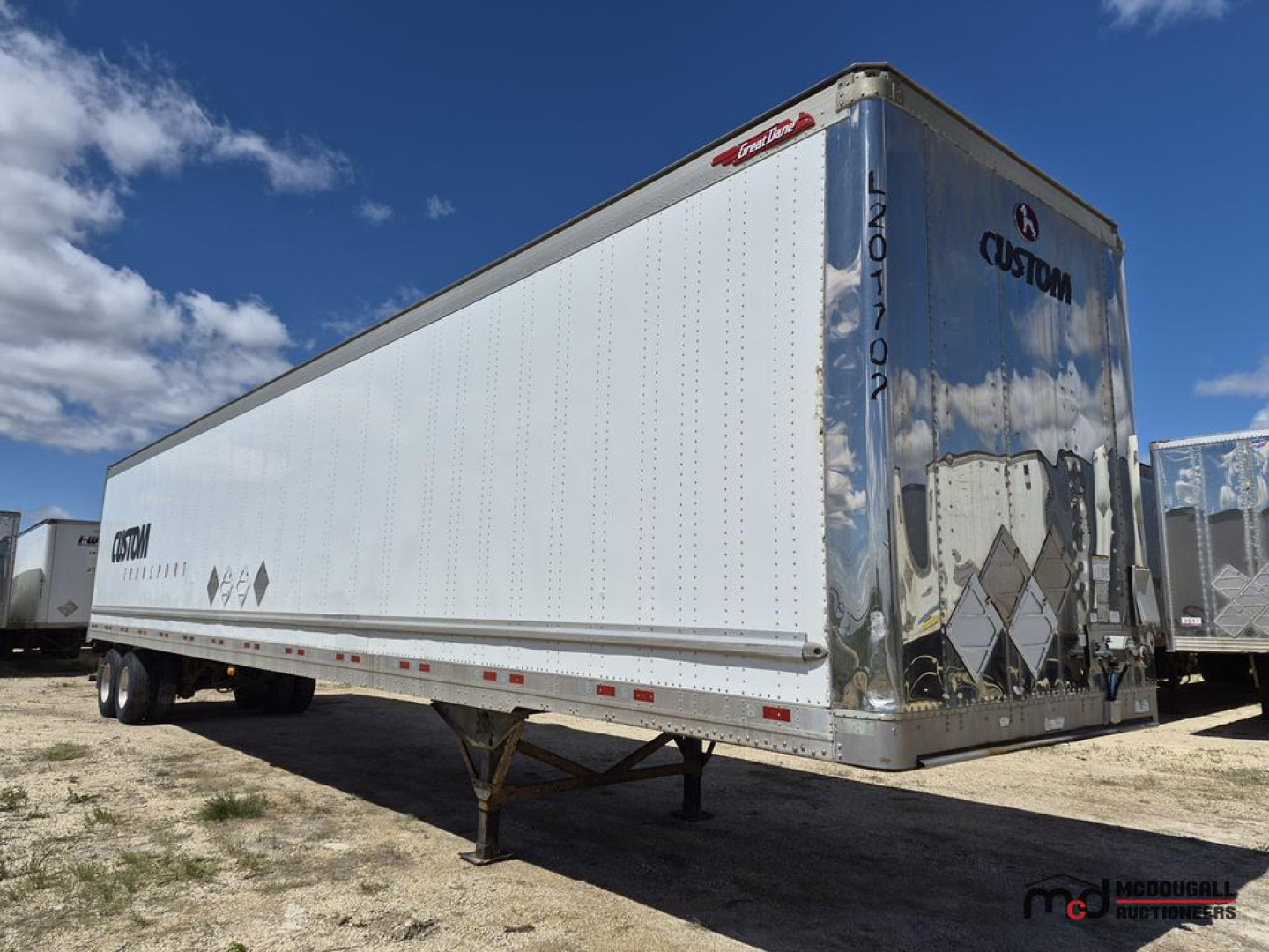 Great Dane 53' dry van semi trailer in silver/blue with Custom logo on rear doors, raised landing gear legs, and DOT/reflective tape along sides.
