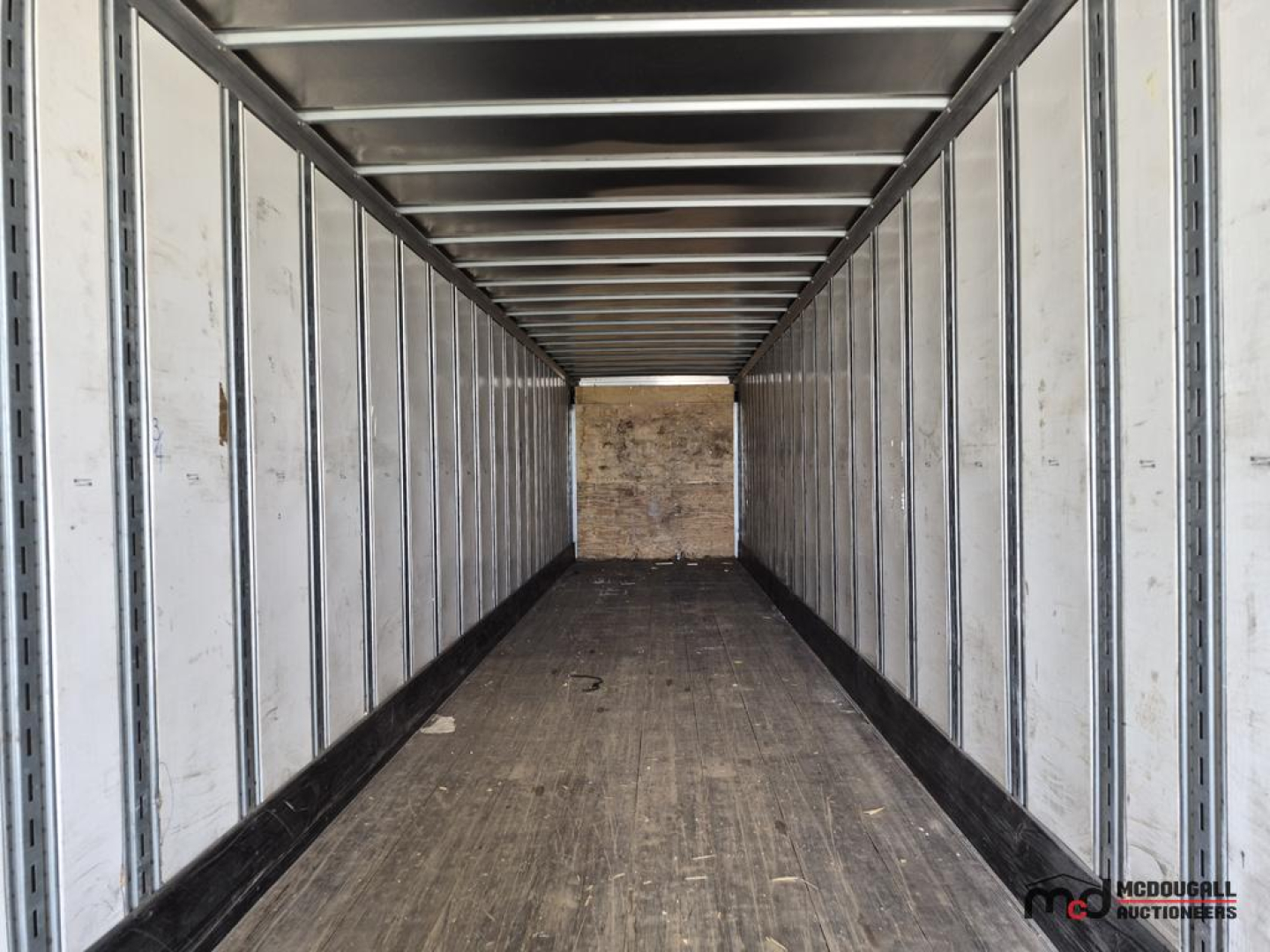 Trailer interior view of a 53' dry van with metal sidewalls and a plywood end wall, empty cargo space.