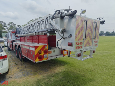 1989 Sutphen aerial tower firetruck with extended ladder and rear platform, red and silver body, keep back 500 feet signage on rear.