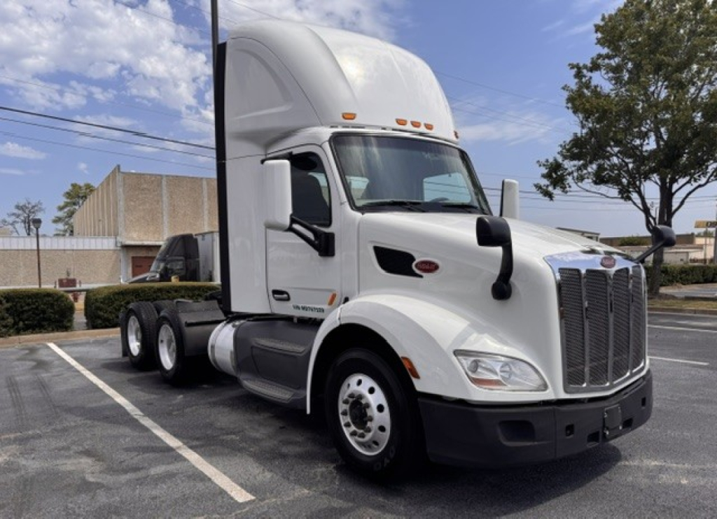 Peterbilt 579 conventional daycab tractor in a parking lot showing front grille, cab, and wheels.