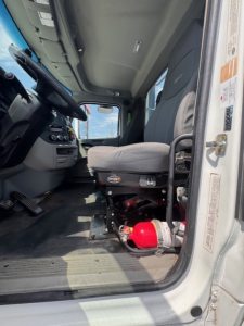 Peterbilt 579 cab interior showing driver seat, steering wheel, dashboard, and red fire extinguisher near floor; VIN sticker area visible on door frame