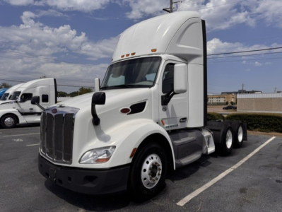 Peterbilt 579 conventional daycab tractor in white, front left view, with sleeper cab raised, dual rear axles, chrome grille.