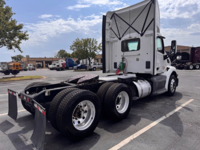 Peterbilt 579 conventional daycab truck rear/side view showing dual rear axles and fifth wheel, with white cab and black chassis.