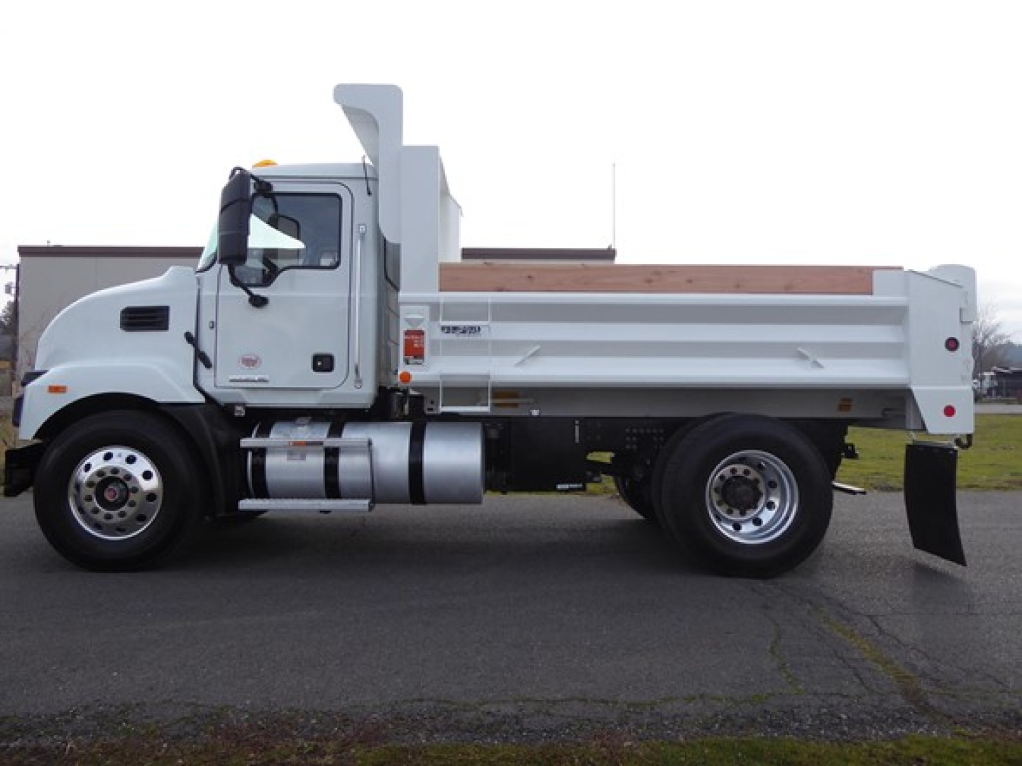 Dump truck side view showing white Mack MD6 dump bed with cargo rails, fuel tank, and rear wheels.