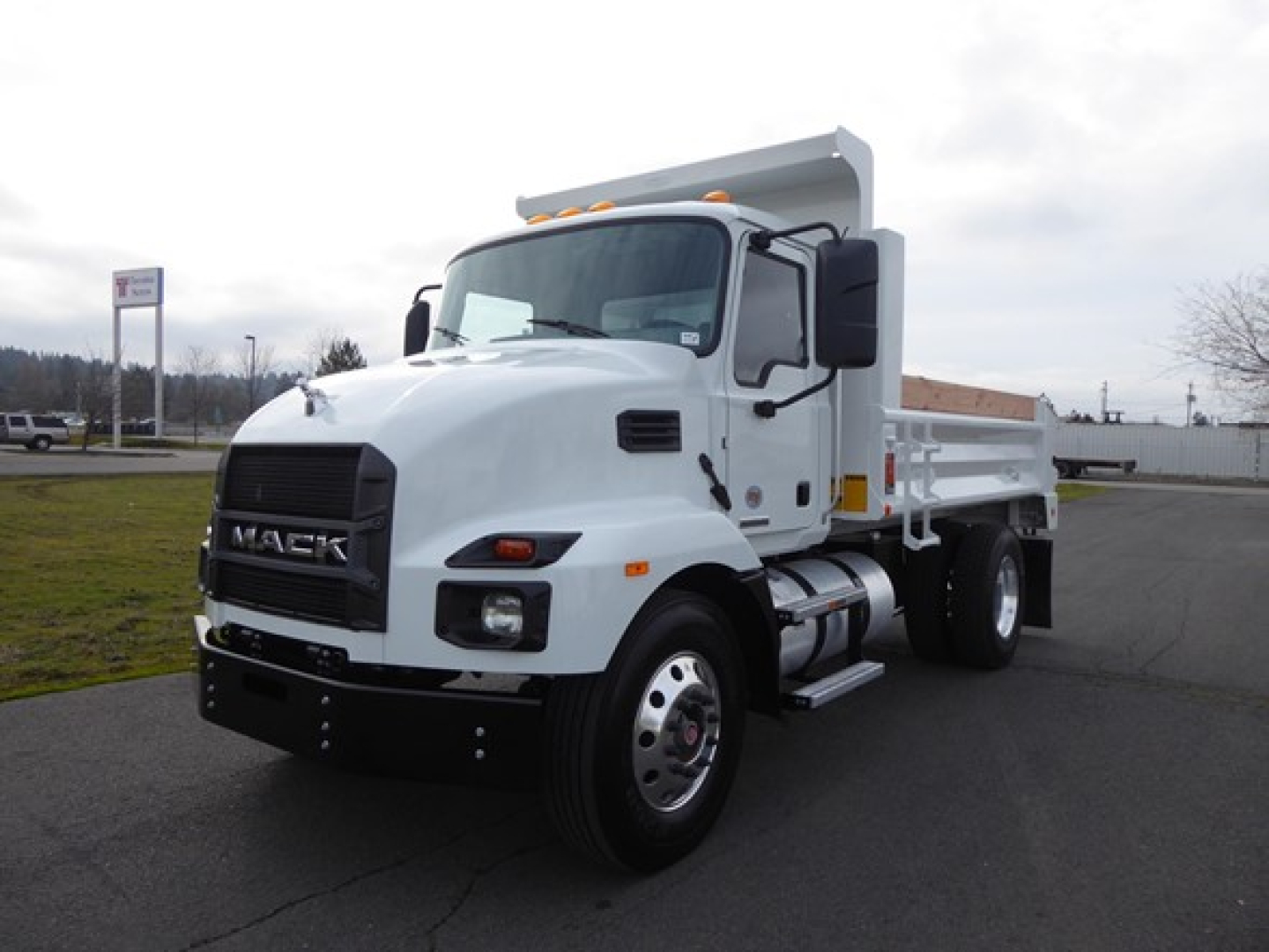 Mack MD6 dump truck in a parking lot, front-left view showing cab and white dump bed.