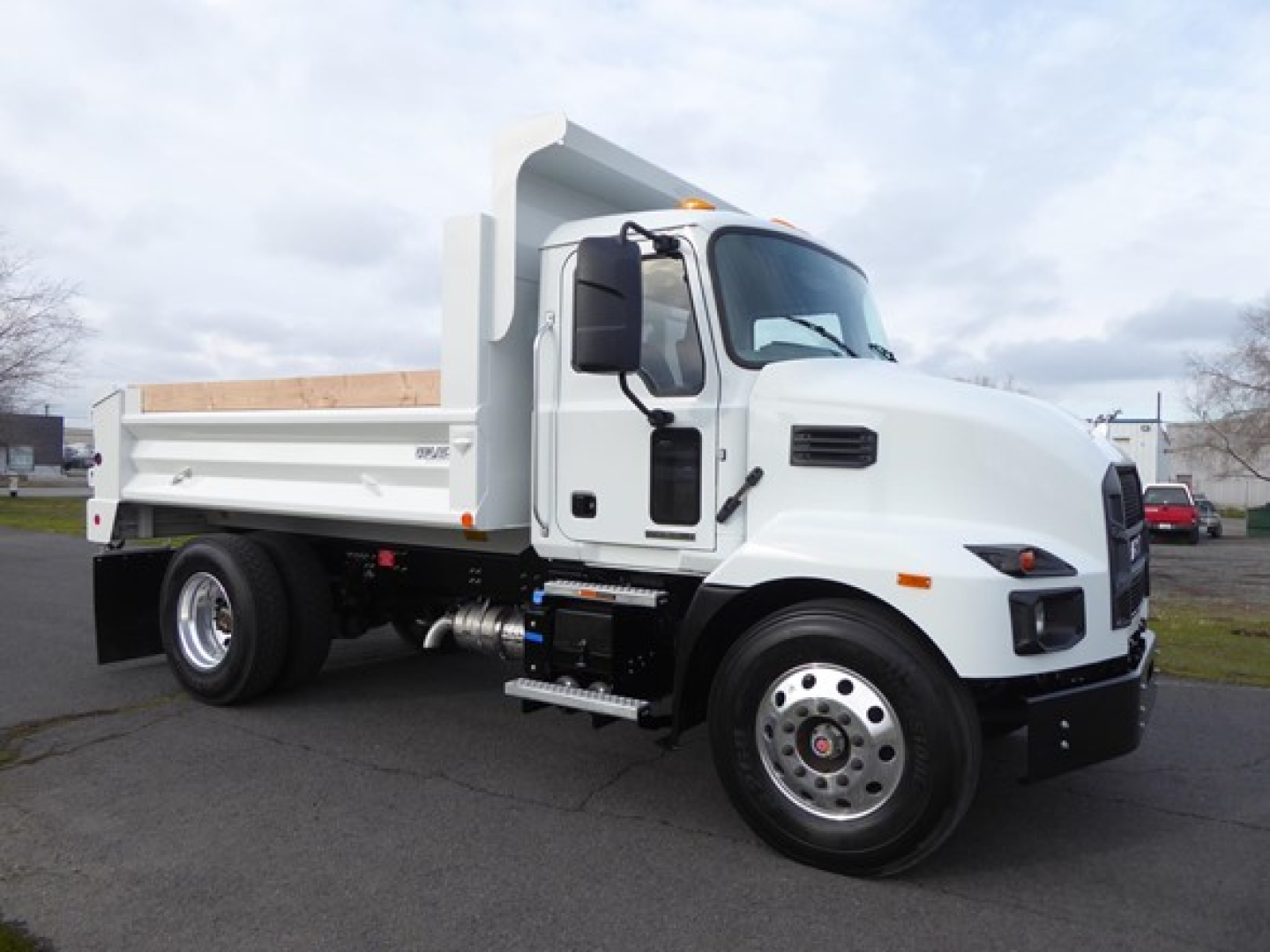 White Mack MD6 dump truck in a parking lot, side view showing dump bed, cab, front wheel, and chrome hubcap. No visible text legible on the truck exterior.