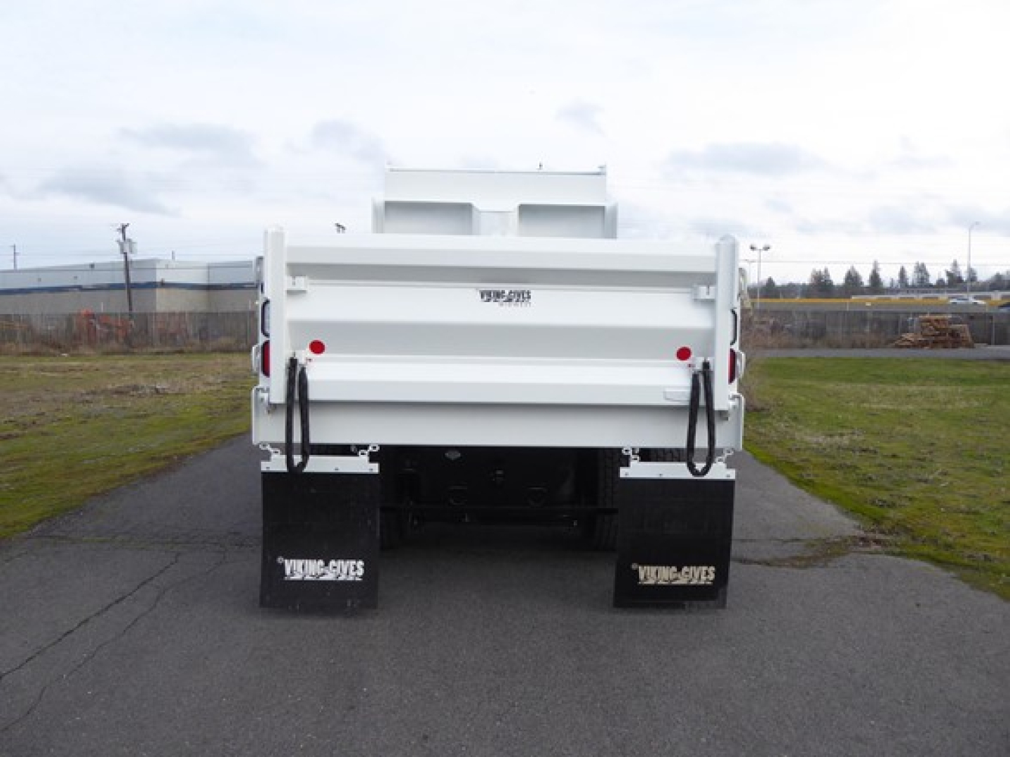 Back view of a white Mack MD6 dump truck showing dual rear-dump bed, black mud flaps with white text, and tailgate area.
