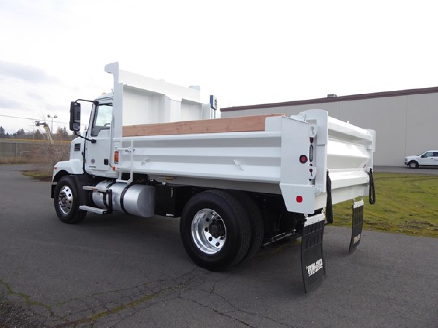 Dump truck side/rear view showing white Mack MD6 dump bed, rear tailgate, and dual rear tires with mud flaps.