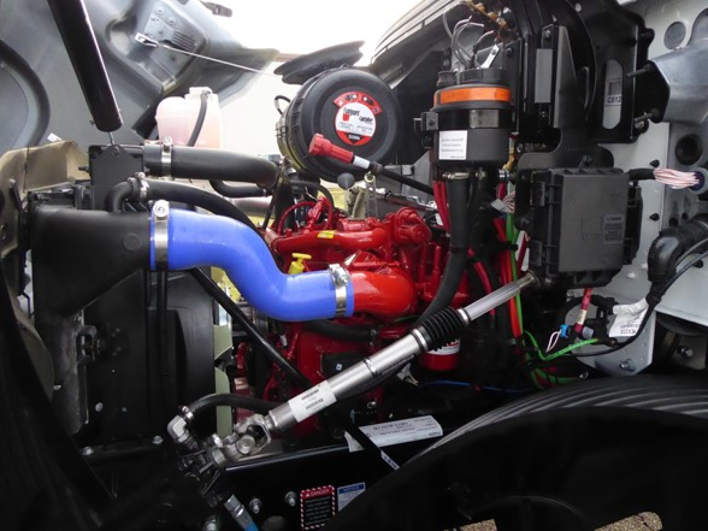 Mack MD6 engine bay showing blue radiator hose, red engine, and various hoses and components.