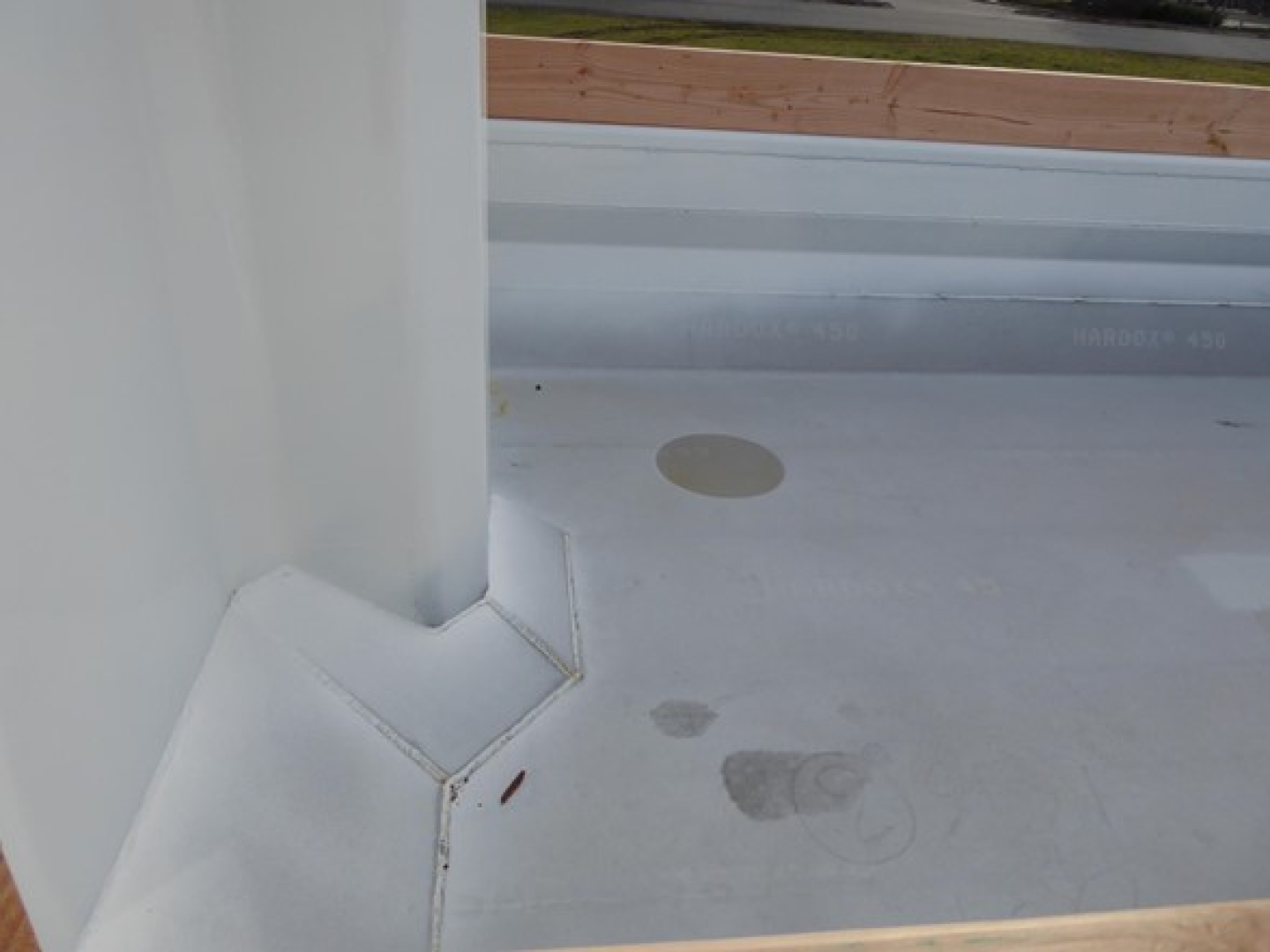 Truck bed surface with white coating showing faint circular footprints and a raised corner seam, view from cabin area.