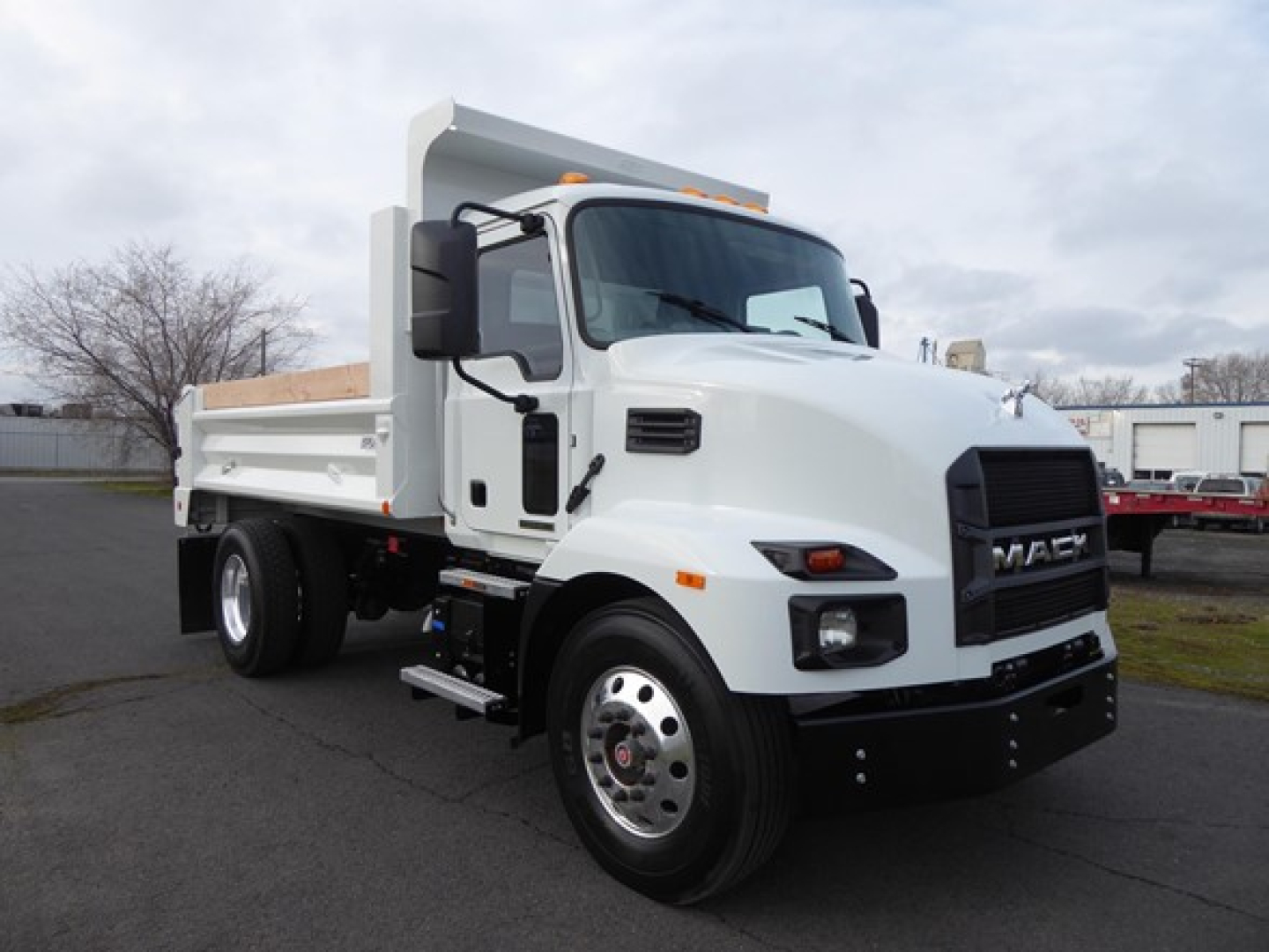 Front-left view of a white 2025 Mack MD6 dump truck showing cab, dump bed, large black grille, and front bumper.