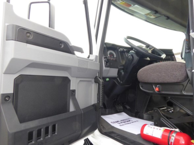 Cab interior of a 2025 Mack MD6 dump truck showing driver seat, steering wheel, dashboard, and open door with steps.