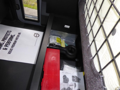 Dump truck cargo area showing a red battery box and towing hitch, with a protective mesh in the side window and documents/paperwork visible.