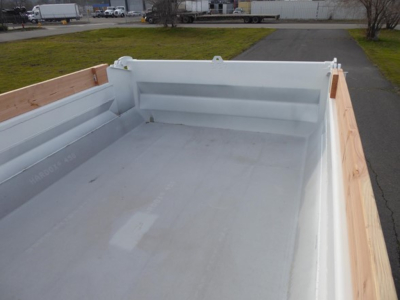 Mack MD6 dump truck bed showing light gray bed liner and wooden side panels, rear view