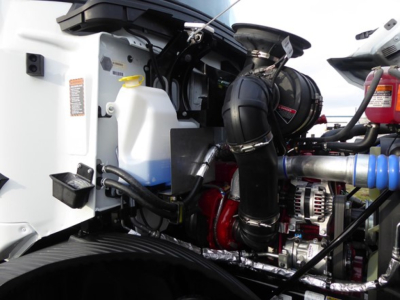 Mack MD6 truck engine bay with visible coolant reservoir, hoses, air intake, and alternator; engine components and tubing in view
